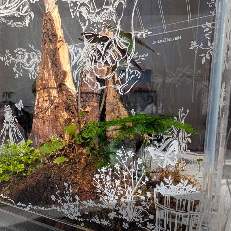 Close-up of the intricate engraving of a mouse celebrating in the trees, with butterflies fluttering around, inside the Victorian-style terrarium.