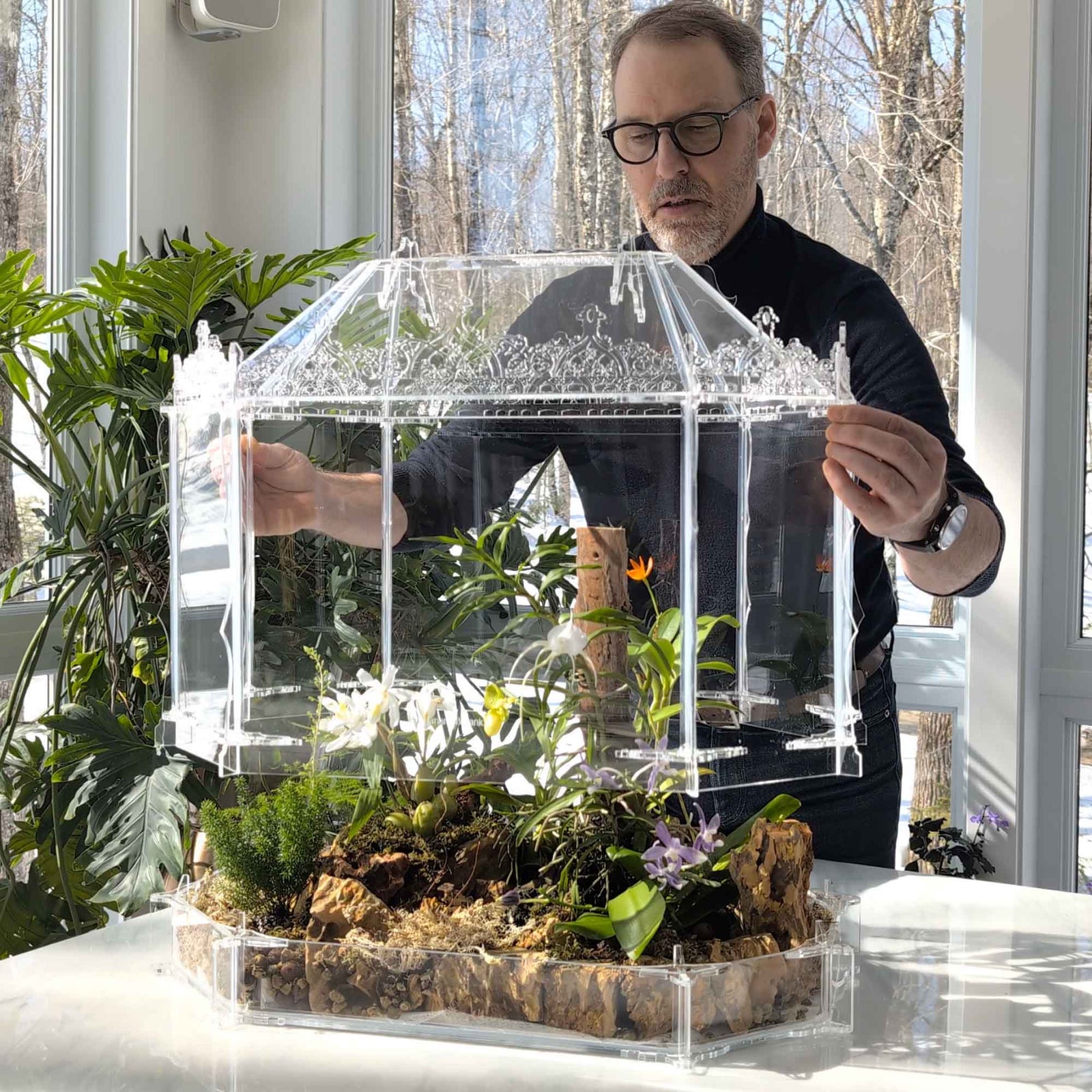 Grand terrarium victorien en acrylique transparent, inspiré du château de Hluboká, abritant des plantes tropicales et de la mousse sous une lumière douce.