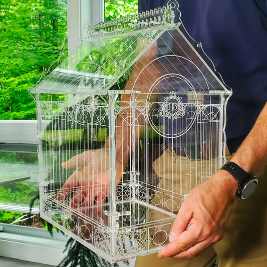 Victorian-style terrarium held in hands, showcasing its intricate acrylic design and elegant greenhouse-inspired structure.